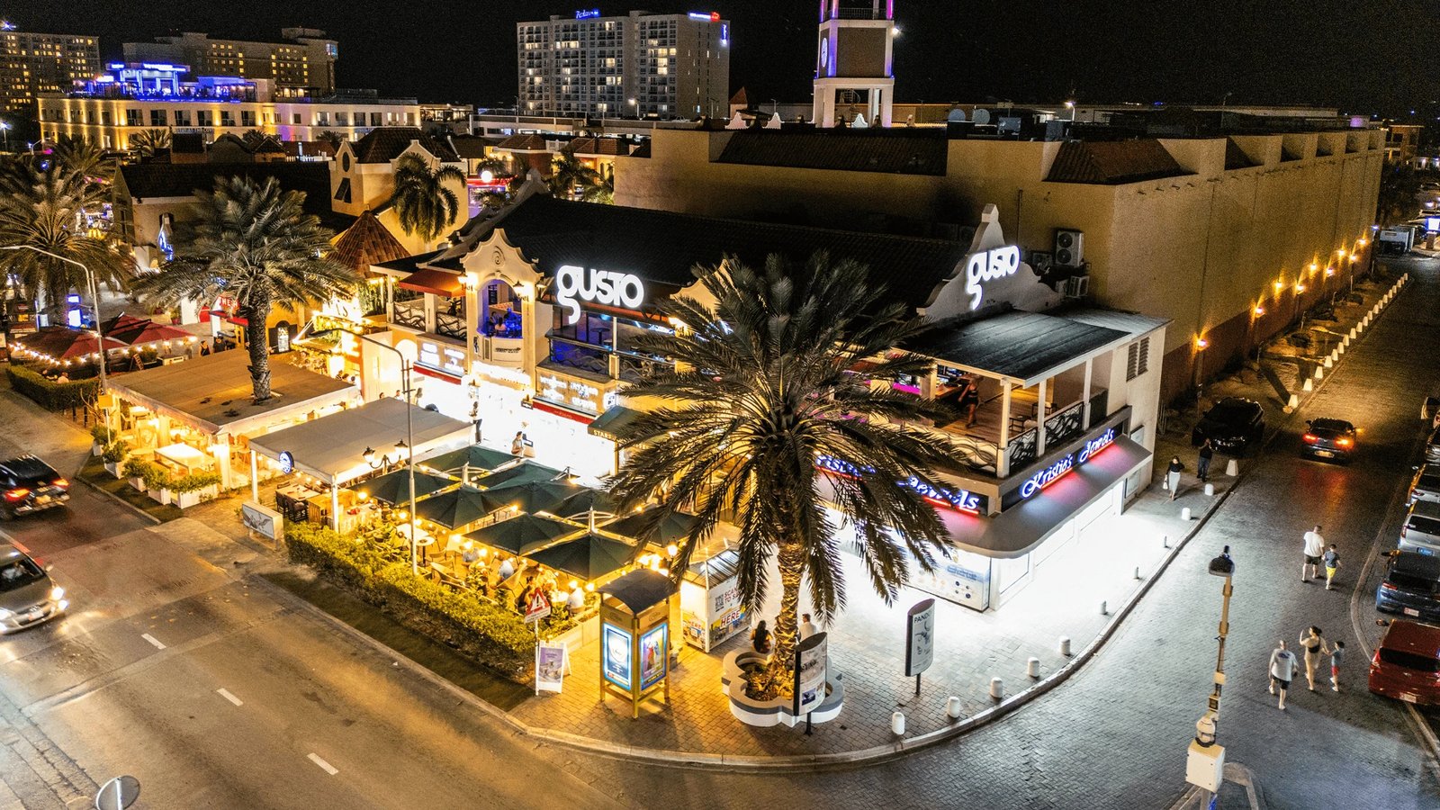 Palm Beach Aruba at night: lit restaurants, terraces and palm trees along the high-rise boulevard